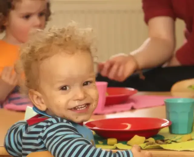 Toddler at TIMS smiling during a Montessori mealtime routine