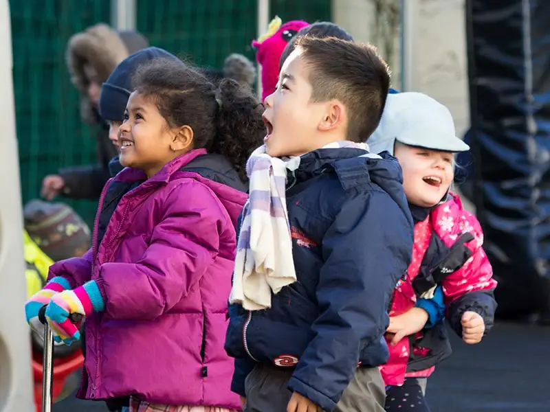 Group of children laughing and looking up excitedly during outdoor play