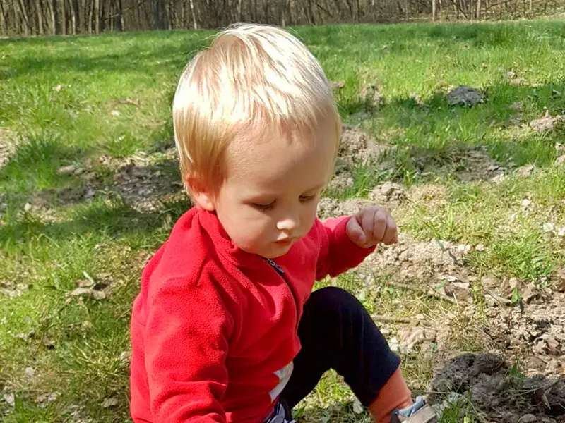 Toddler crouching in the grass exploring soil during outdoor play