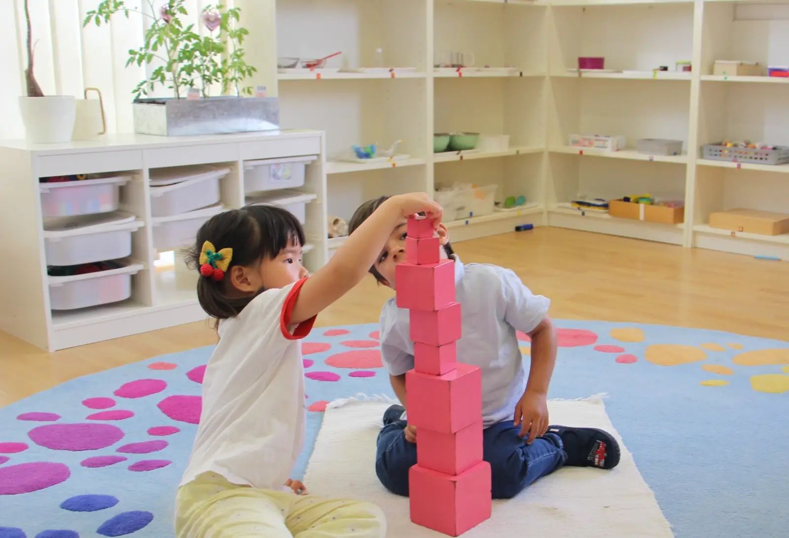 Two children stacking the Montessori pink tower blocks together