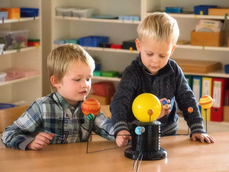 Two boys examining a solar system model at a classroom table